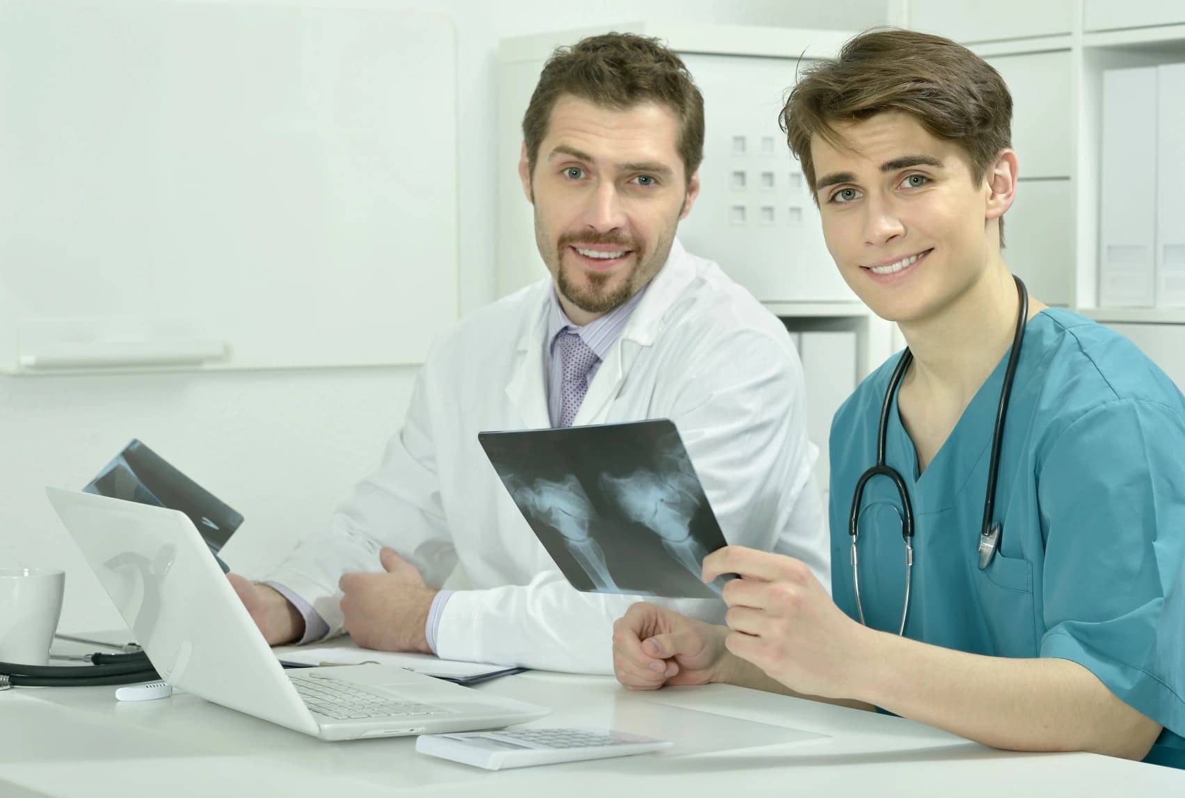 Two smiling orthopedic clinicians at a desk holding up a knee X-ray