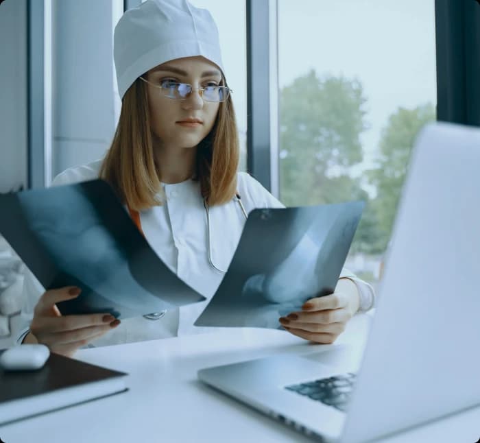 Medical coder comparing two trauma X-ray films beside a laptop at a desk