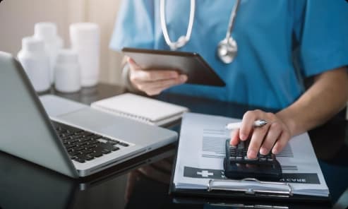 Clinician reviewing billing paperwork with a laptop and calculator