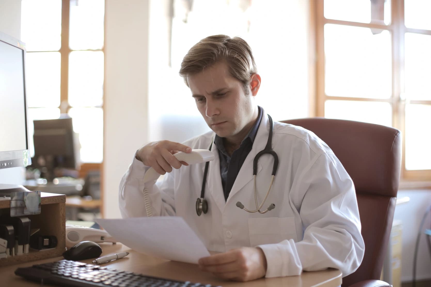 Physician at a practice desk reviewing a claim document while on the phone