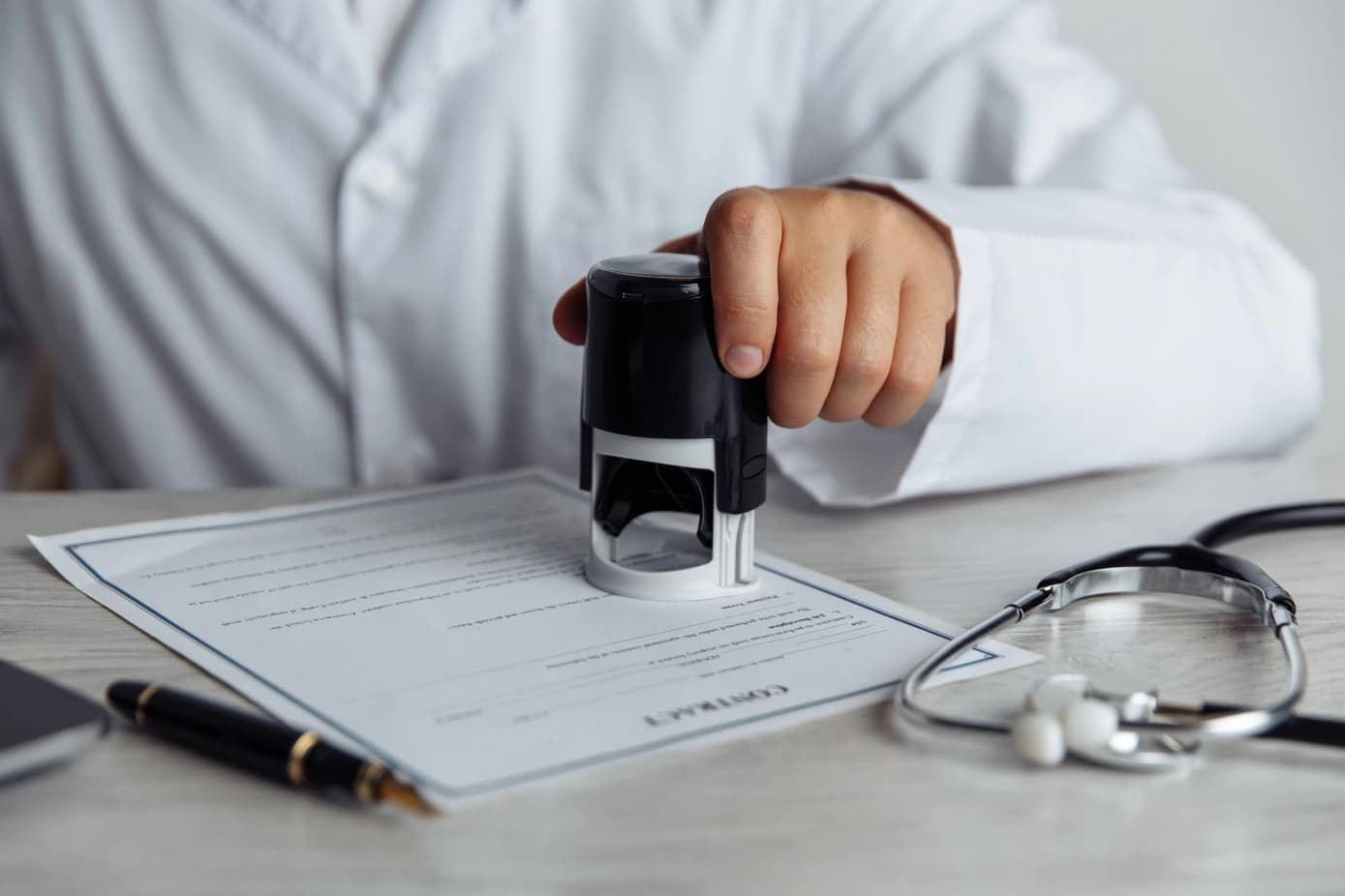Physician stamping an approved authorization form beside a stethoscope on a clinic desk