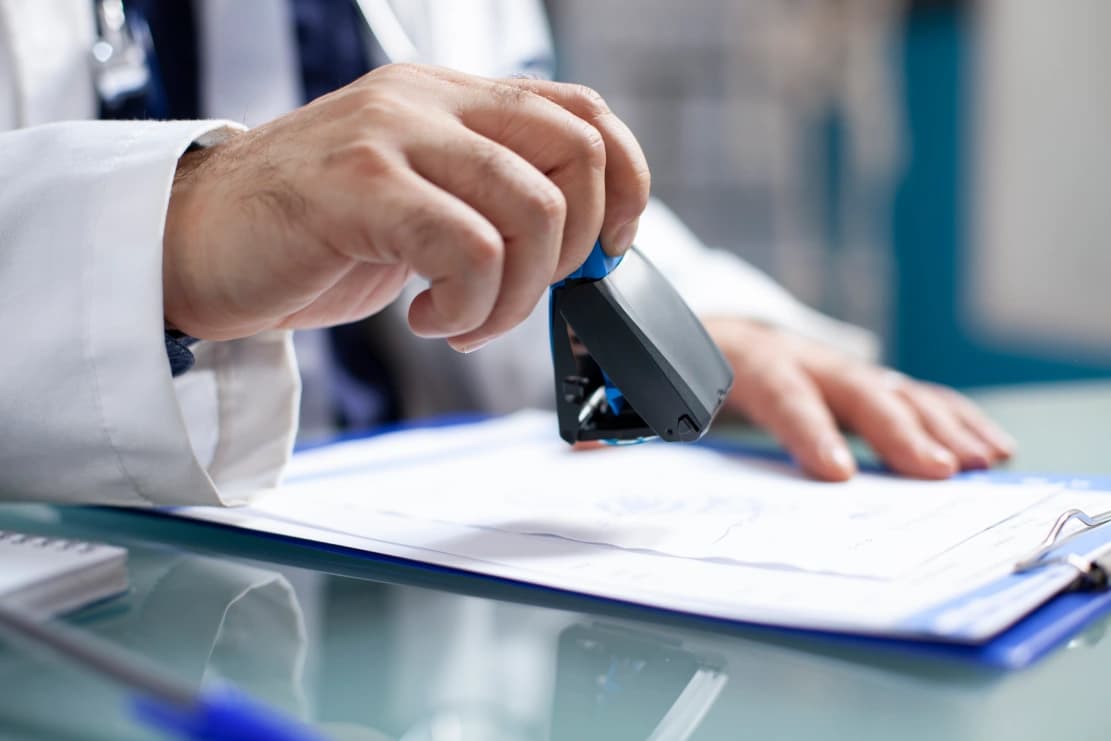 Physician stamping a provider credentialing document on a clipboard