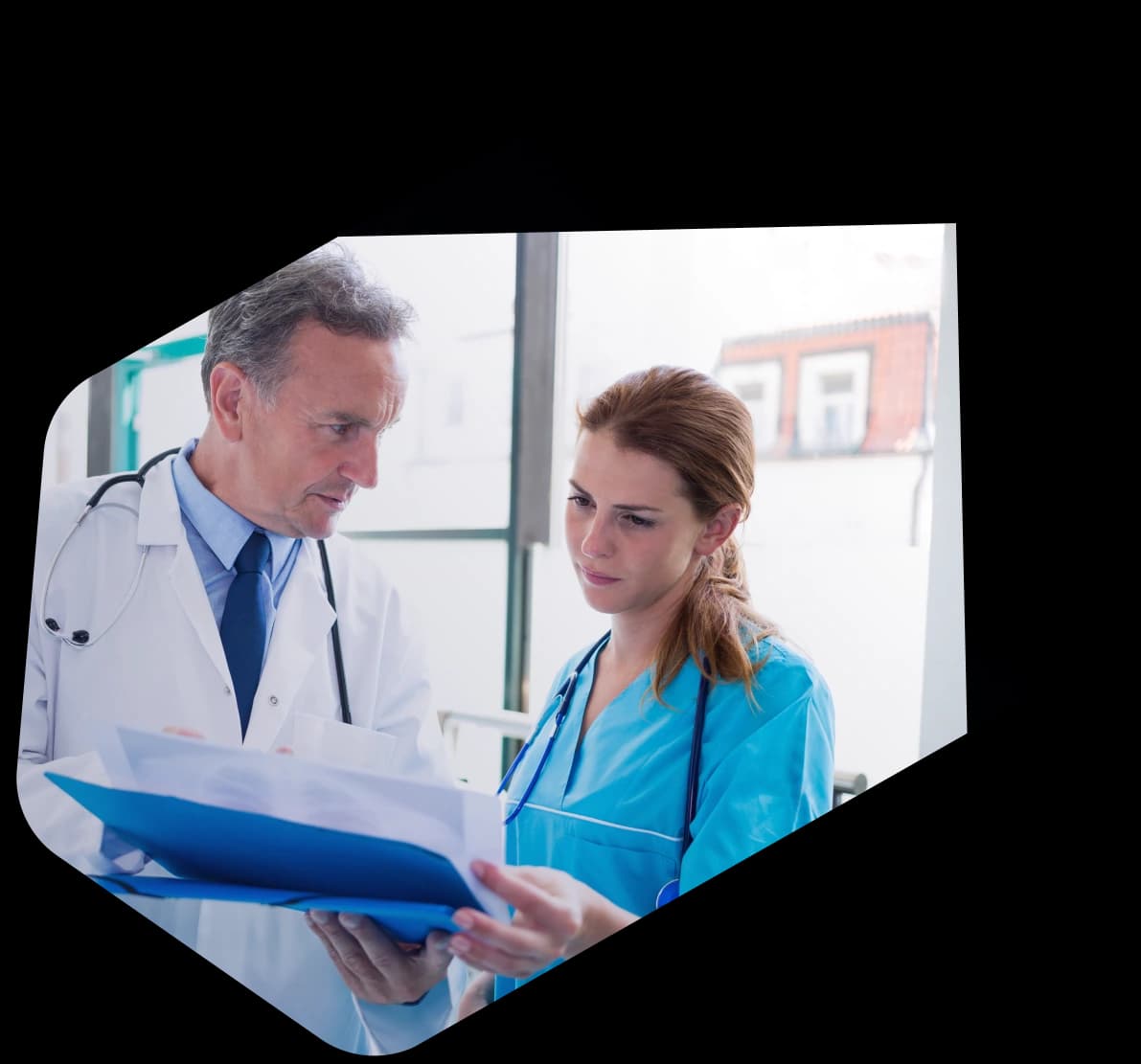 A physician in a white coat and a nurse in blue scrubs reviewing prior authorization paperwork together on a clipboard