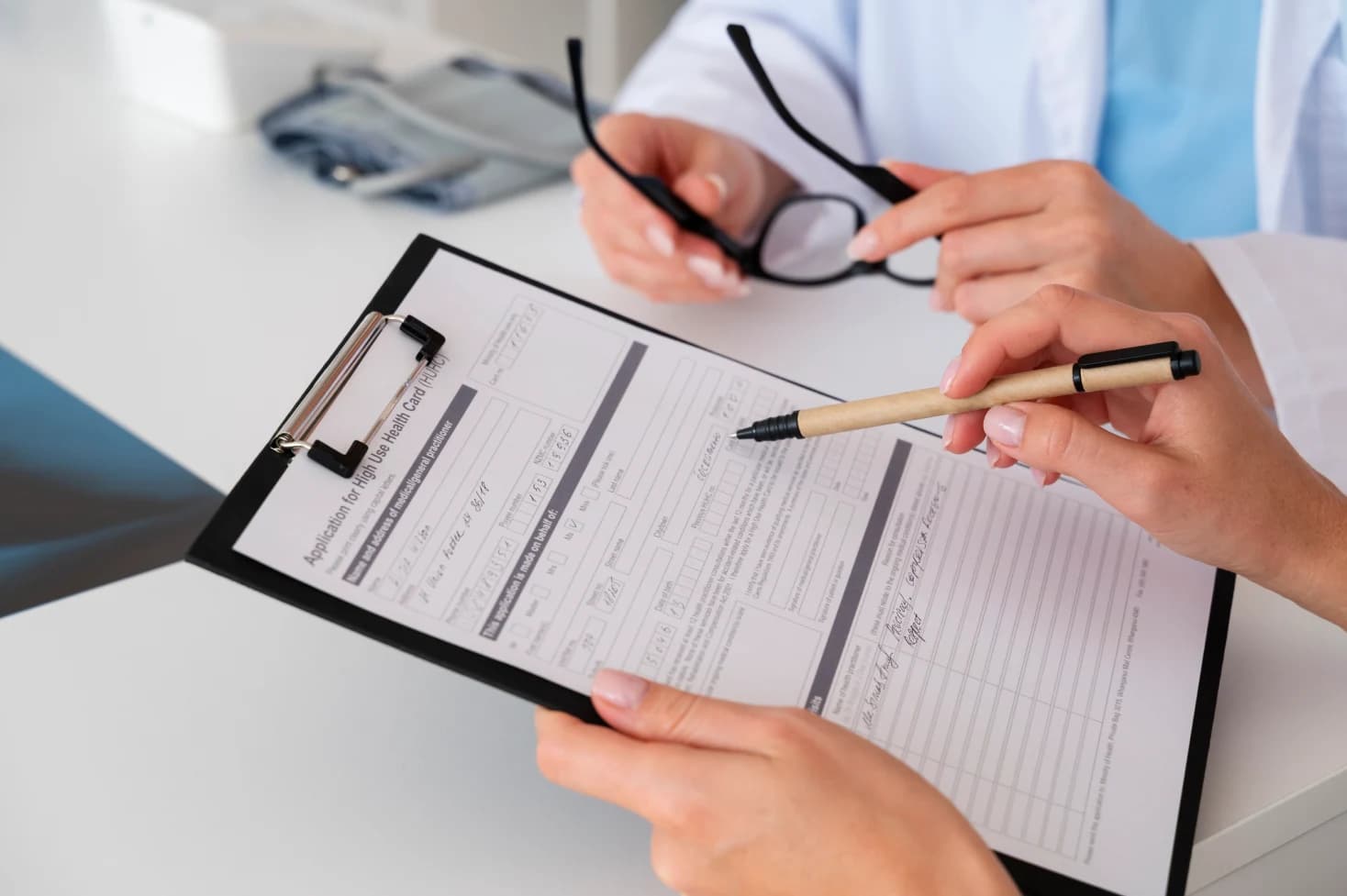 Patient at a clinic desk filling in a prior authorization consent form while a staff member points to the signature line